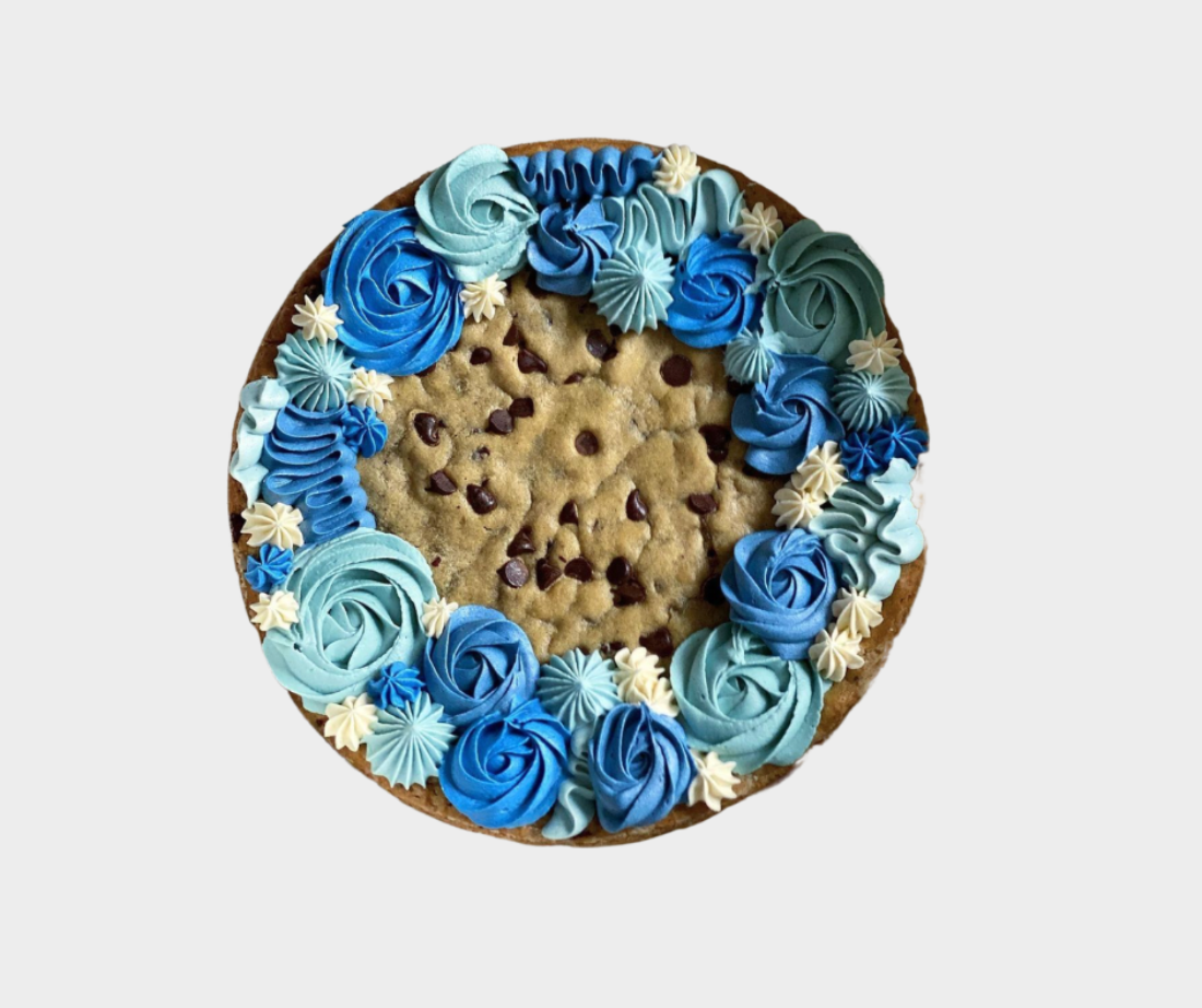 Chocolate chip cookie cake with hues of blue frosting on a cookie background